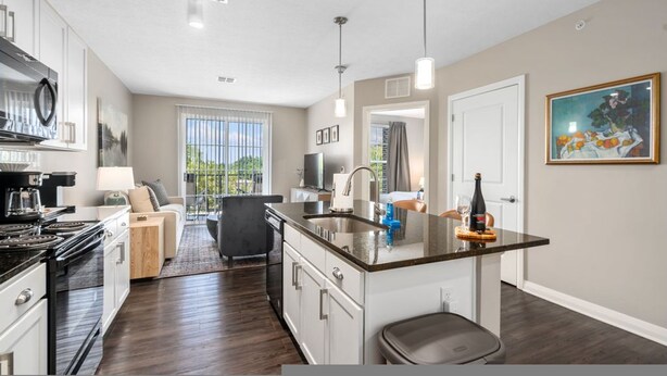 A modern kitchen with a central island, a dining area with a sofa, and a view of greenery outside. - The Urban Loft Free Parking 9 Minutes To OSU (Columbus)