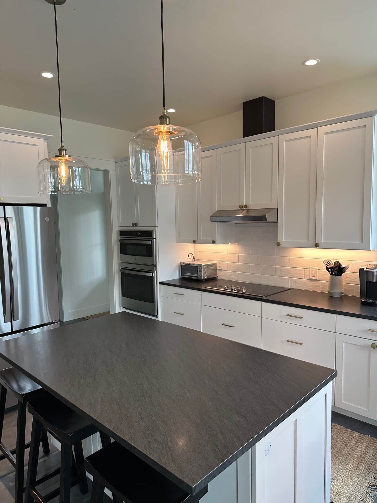 A modern kitchen with white cabinets, a stainless steel refrigerator, a built-in oven, and a dark countertop.
