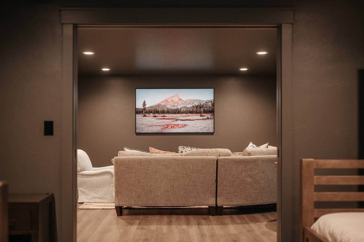 A cozy room with a large flat-screen TV mounted on the wall, a beige sofa, and a wooden chair.