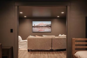 Um quarto aconchegante com uma grande TV de tela plana na parede, um sofá bege e uma cadeira de madeira.