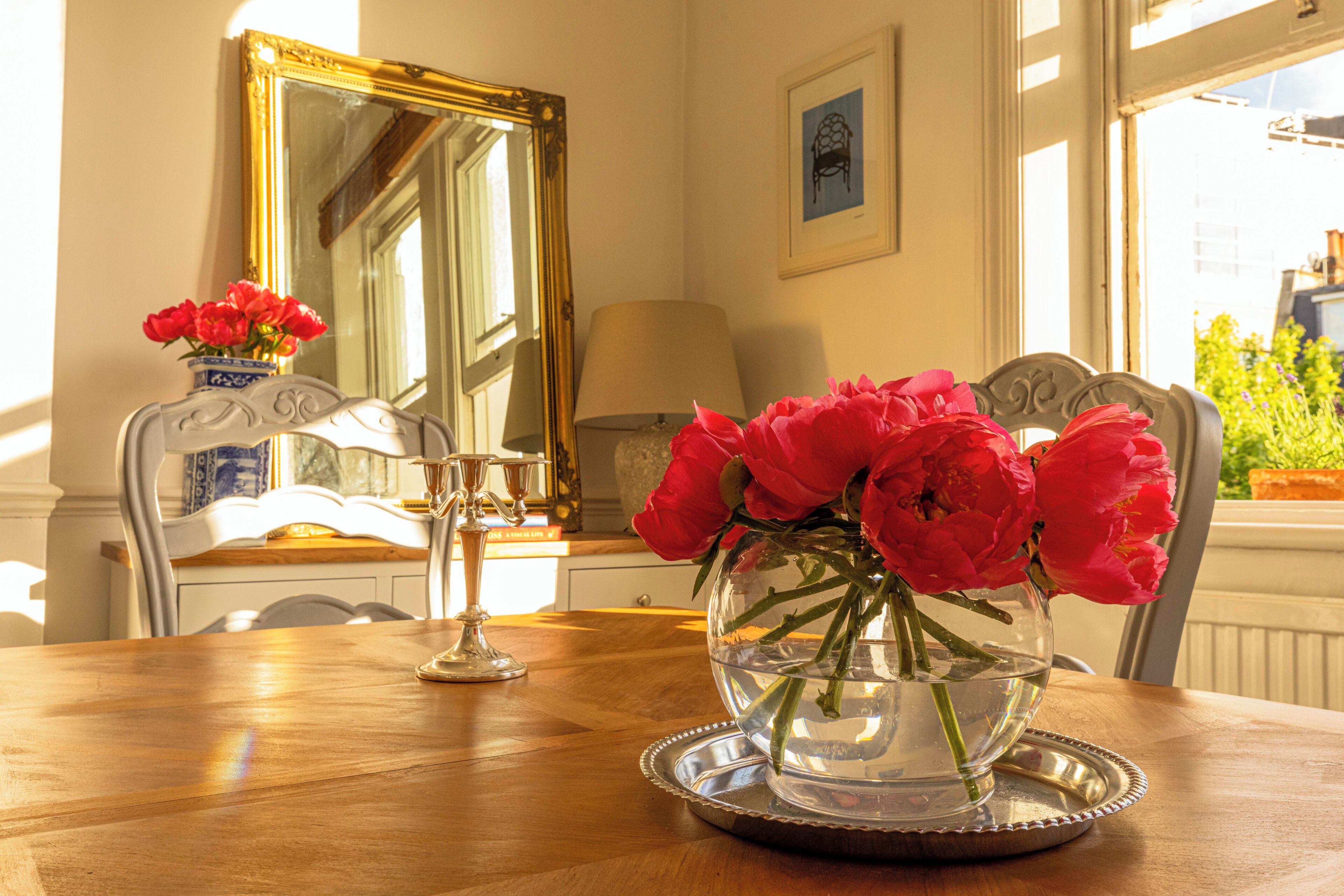 A dining table with a clear glass vase containing red flowers, a silver tray, and a blue and white vase with red flowers.