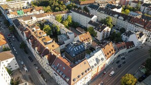 An aerial view of a cityscape with a mix of residential and commercial buildings, a central square, and a busy street with vehicles. - Conlon House Lower East Side (Munich)