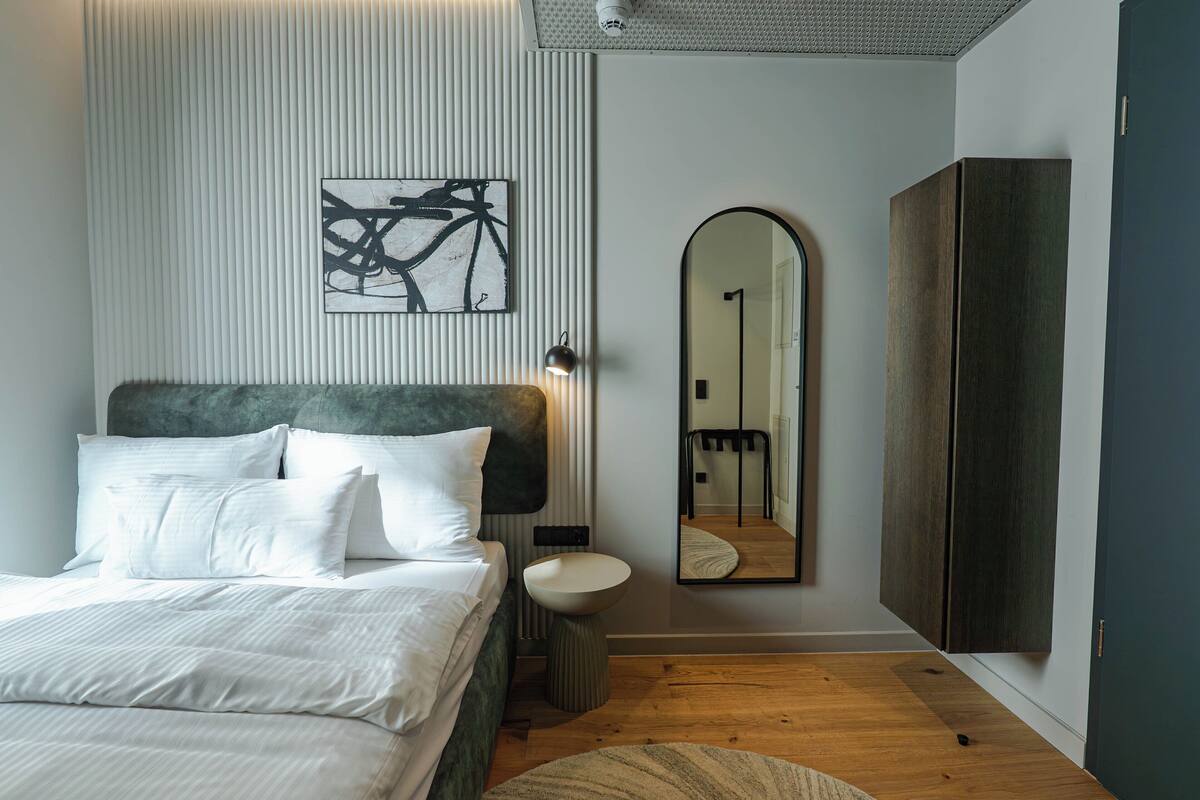 A modern bedroom with a bed, a bedside table, a mirror, and a wardrobe.