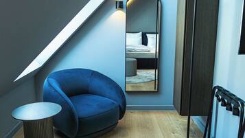 Un dormitorio moderno con techo inclinado, una silla azul, un espejo redondo y suelo de madera.