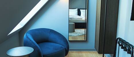 Une chambre à coucher moderne avec un plafond en pente, une chaise bleue, un miroir rond et un plancher en bois.
