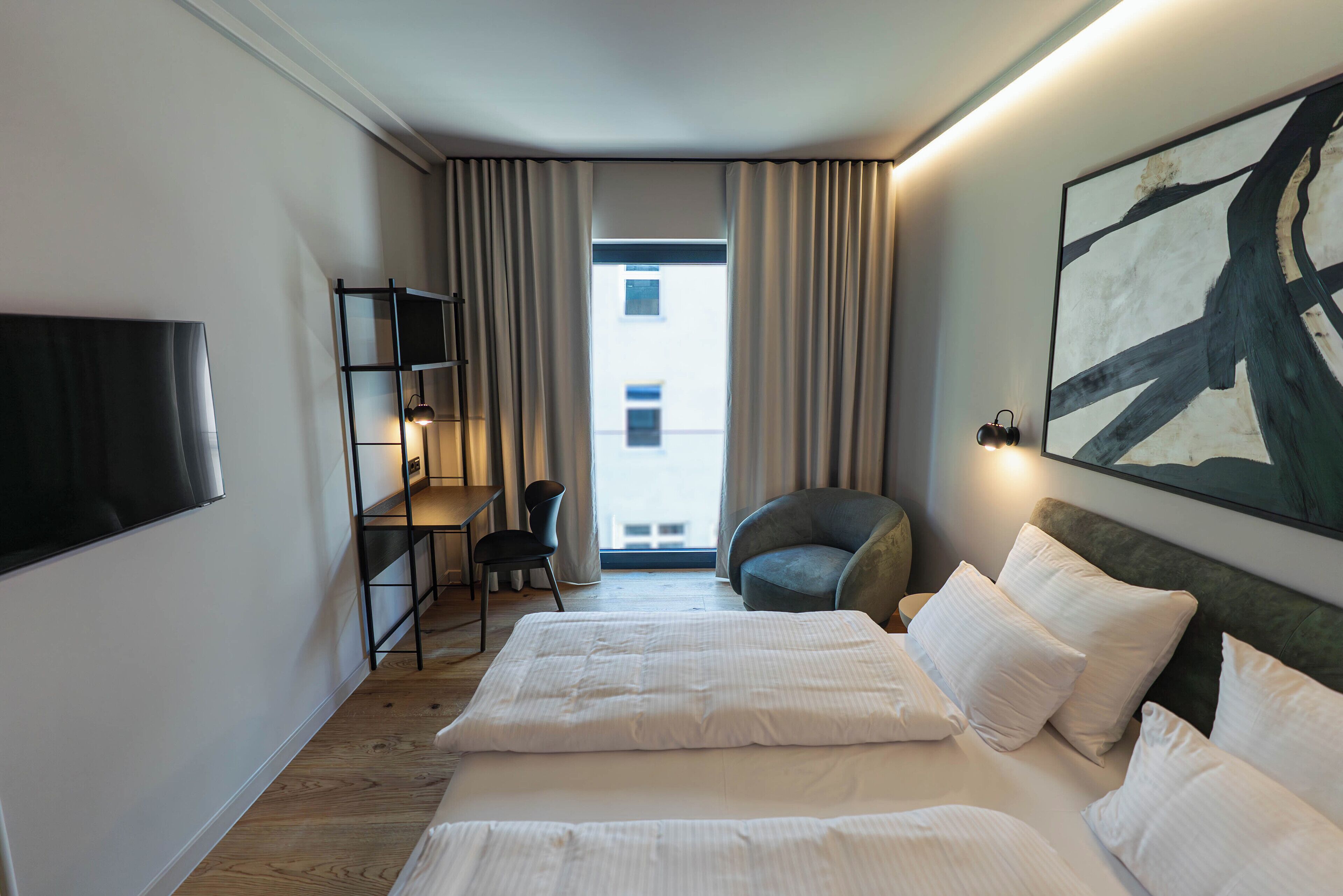 Habitación de hotel con cama, escritorio, silla, televisor y un cuadro abstracto grande en la pared.