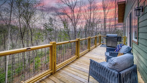 A wooden deck with a metal railing, a grill, and a sofa with cushions. - Charming Mountain Home- Gather, Relax, Explore (Ranger)