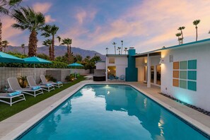Piscina com espreguiçadeiras, área de estar no pátio e um edifício com design moderno.