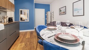 A modern kitchen with wooden cabinets, a marble countertop, and a dining area with a blue chair, white table, and red and white plates. - [Lakeside] New two-room apartment 2 (Como)