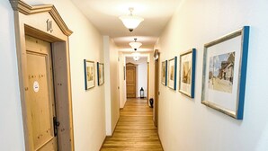A hallway with wooden flooring, framed pictures on the walls, and a door with a number plaque. - Hotel Albers (Recklinghausen)