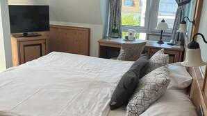 A neatly made bed with pillows, a television on a wooden cabinet, a small table with a lamp, and a window with curtains. - Hotel Albers (Recklinghausen)