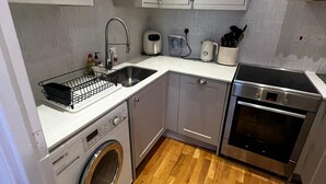 Una cucina compatta con mobili bianchi, lavatrice, forno integrato e lavello.