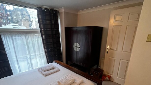 Una camera d'albergo con un letto, un armadio in legno scuro, una porta bianca e una finestra con tende.