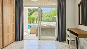 Una stanza con un'armadietto in legno, una scrivania, una sedia e vista su una piscina attraverso una porta vetrata.