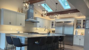 A modern kitchen with a central island, bar stools, a stainless steel refrigerator, and pendant lighting.