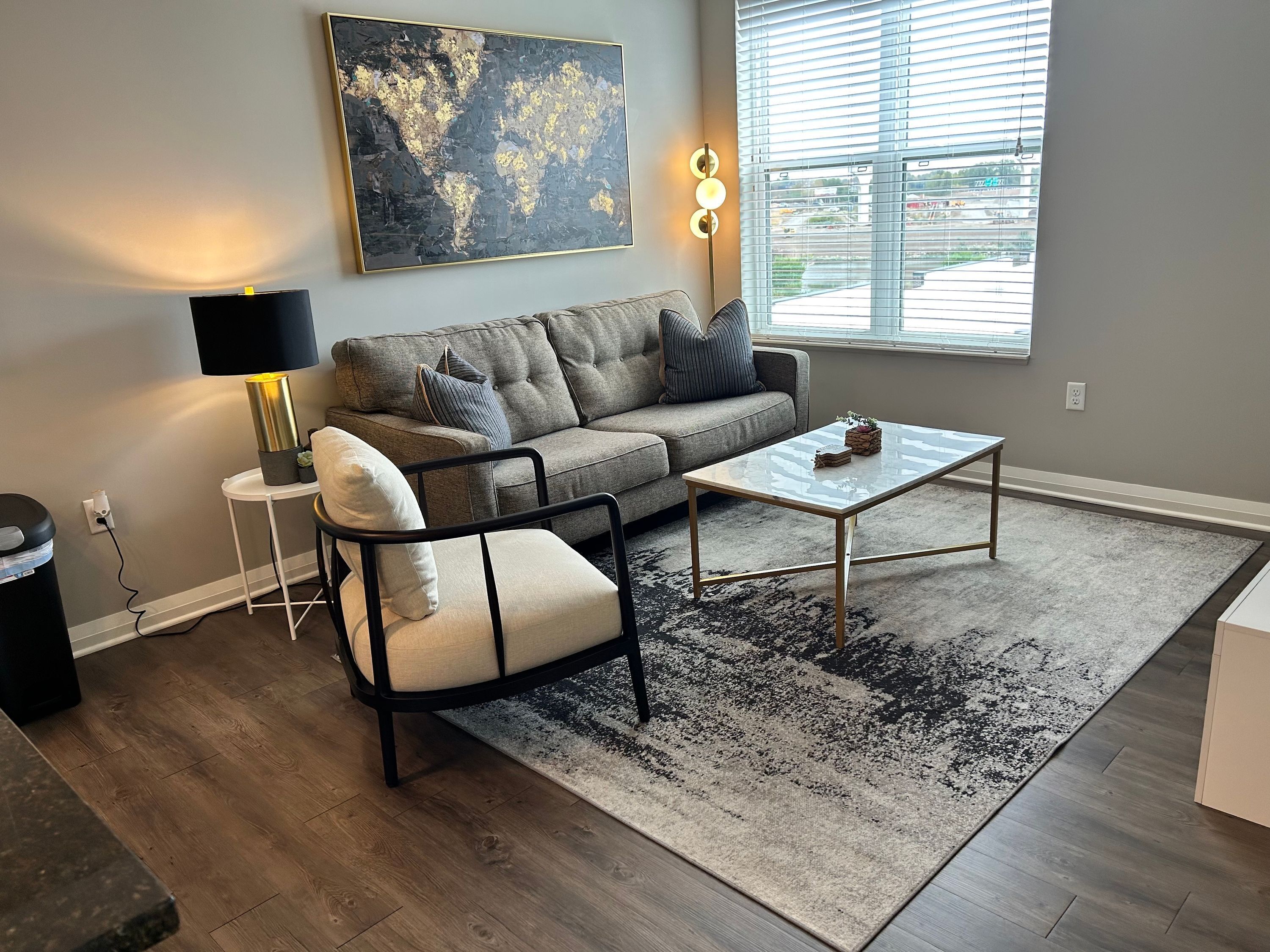 A modern living room with a grey sofa, a black and white armchair, a glass coffee table, and a large abstract painting on the wall.
