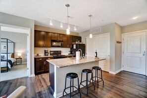 A modern kitchen with dark wood cabinets, a granite countertop, and a central island with bar stools. - Downtown Designer 2BR Parking W D Gym Pool (Columbus)