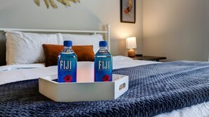 Ein Hotelzimmer mit einem Bett, Kissen, einem Tablett mit zwei Fiji Wasserflaschen und einem Wandbild.
