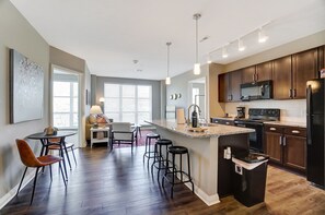 A modern kitchen with dark wood cabinets, a large island with bar stools, and a dining area with a round table and chairs. - Downtown Designer 2BR Parking W D Gym Pool (Columbus)