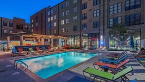 A swimming pool with lounge chairs and tables, surrounded by multi-story buildings with large windows. - City View 2BR Free Parking Pet-friendly (Columbus)