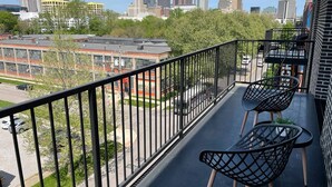 Un balcone con due sedie nere, vista su un panorama urbano con diversi edifici, tra cui una torre imponente, e un parcheggio con alcune auto.