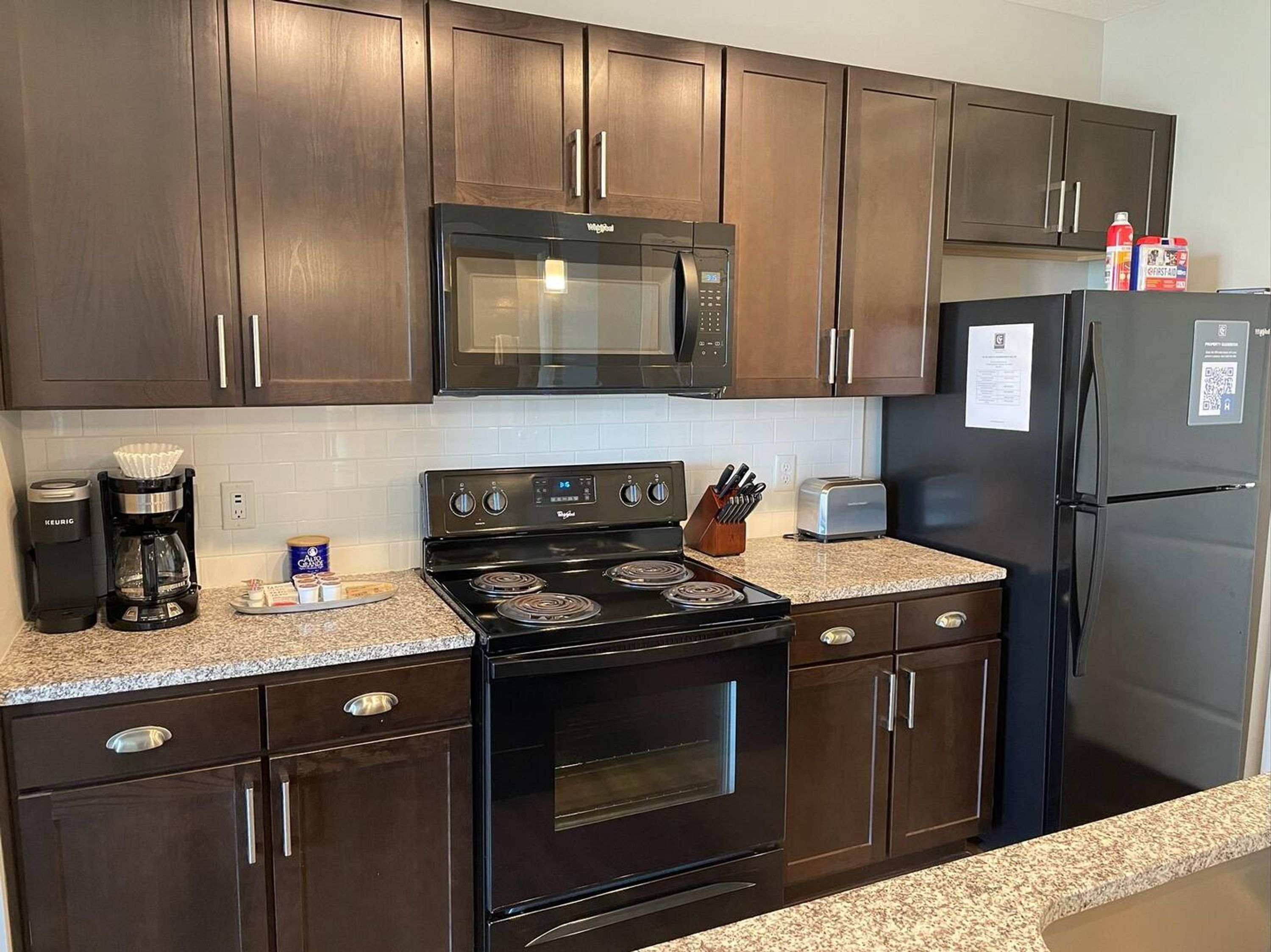 A modern kitchen with dark wood cabinets, a black microwave, a stove, a refrigerator, and a coffee maker.