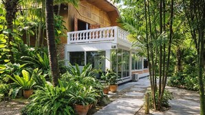 Ein Holzhaus mit einem Balkon, umgeben von üppiger Vegetation und Topfpflanzen.