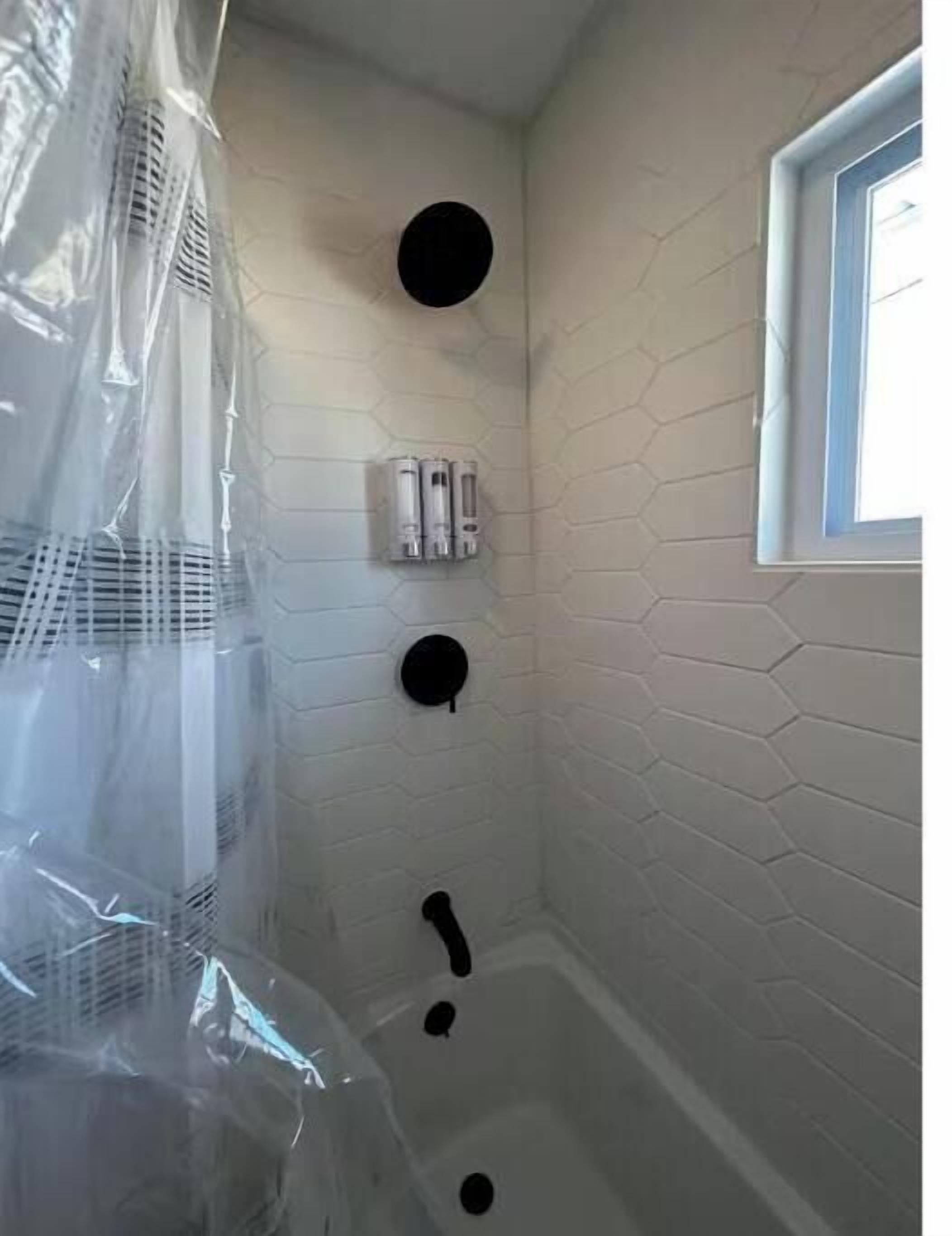 Un baño con pared de ladrillo blanco, una ventana y una cortina de ducha.