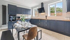 Una cocina moderna con armarios oscuros, una mesa de comedor preparada para cuatro comensales y un ventanal que proporciona luz natural.