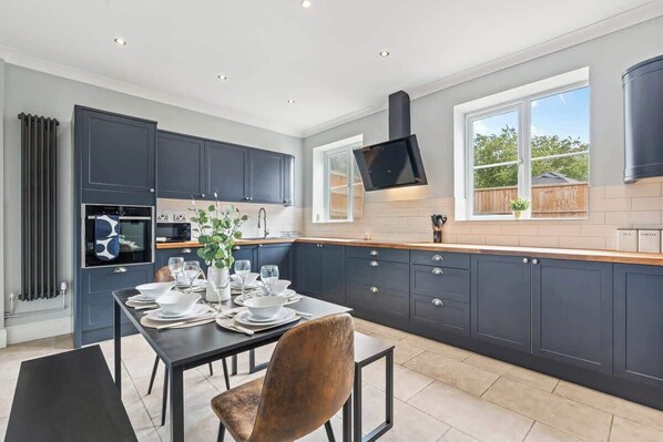A modern kitchen with dark cabinetry, a dining table set for four, and a large window providing natural light.