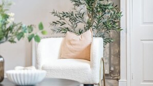 Un sillón blanco con cojín beige, una mesa redonda con un bol blanco y una planta en maceta con hojas verdes.