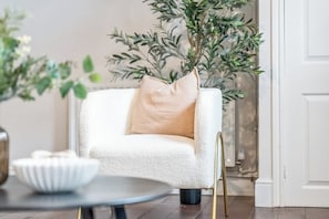 A white armchair with a beige cushion, a round table with a white bowl, and a potted plant with green leaves. - Inviting & Charming Home | Free Wi-Fi | Sleeps 8 (Newark-on-Trent)