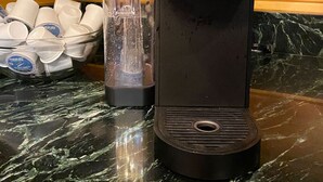 En Keurig-kaffemaskine på en marmorbordplade med en glaskande og en kurv med engangskopper.