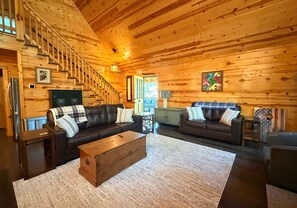 A log cabin interior with a staircase, two sofas, a coffee table, and a dining area.