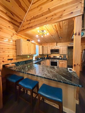 A kitchen with wooden cabinets, a marble countertop, and a bar area with stools.