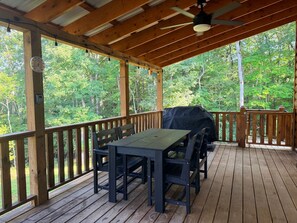 A covered outdoor deck with a table and chairs, a ceiling fan, and a grill.