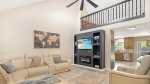 A spacious living room with a beige sofa, a flat-screen TV, and a fireplace.