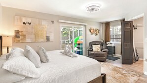 A bedroom with a large bed, a chair, a door, and a window.