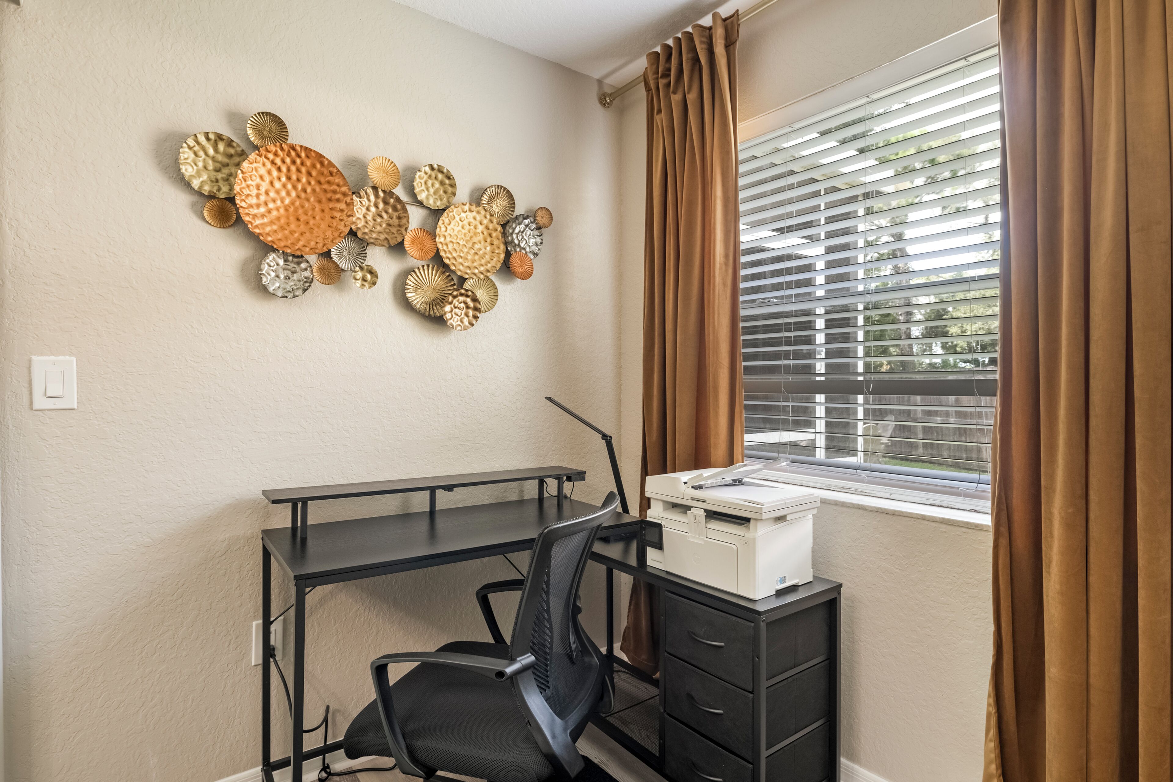 A workspace with a desk, chair, printer, and decorative wall art.