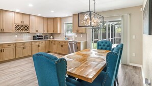 A modern kitchen with wooden cabinets, a dining table with blue upholstered chairs, and a chandelier.
