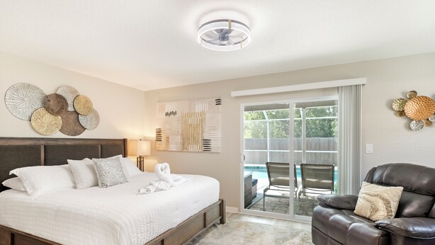 A bedroom with a large bed, a leather chair, and a view of the outside.