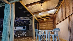 An outdoor wooden deck with a table and chairs, a hanging light fixture, and a wooden wall. - Country House with Waterfall and Pool - Maciambu Waterfall - Country House (Enseada de Brito)