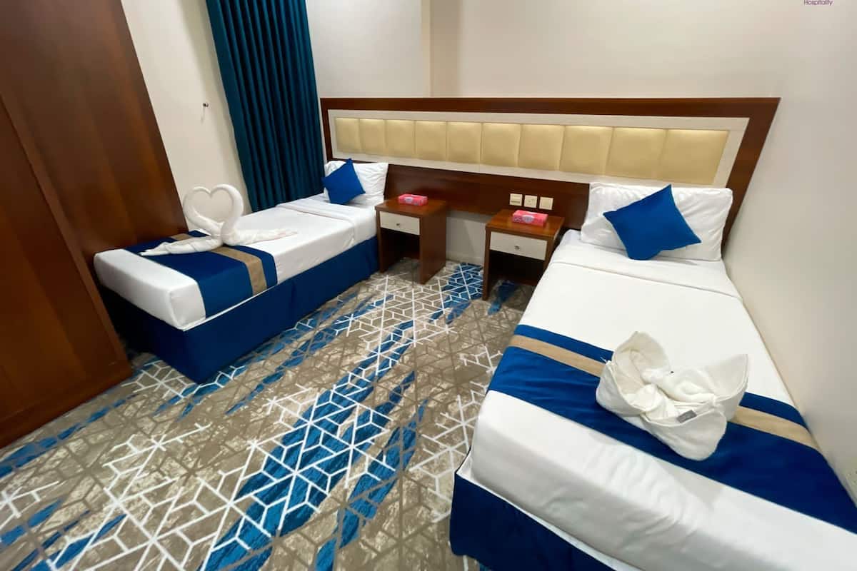 Ein Hotelzimmer mit zwei Betten, einem Holz-Kopfteil, einem gemusterten Boden und einem blauen Vorhang.