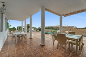 Un área de patio techada con columnas blancas, una piscina y mobiliario exterior.