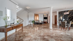 Amplia sala de estar con piso de mármol, una mesa de comedor con sillas, un sofá y una escalera.
