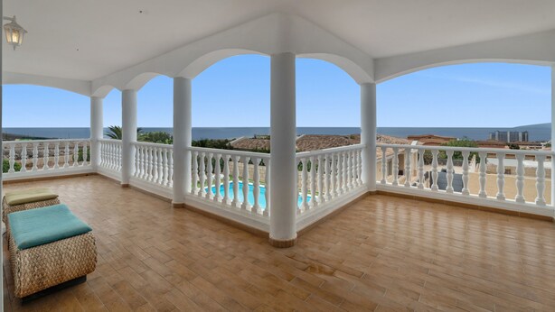 Un espacio al aire libre cubierto con piscina, columnas blancas y vistas al mar.