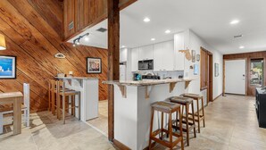 A modern kitchen with white cabinets, a central island with stools, and wooden beams on the ceiling. - Sea Dunes Green Turtle A3 (New Smyrna Beach)