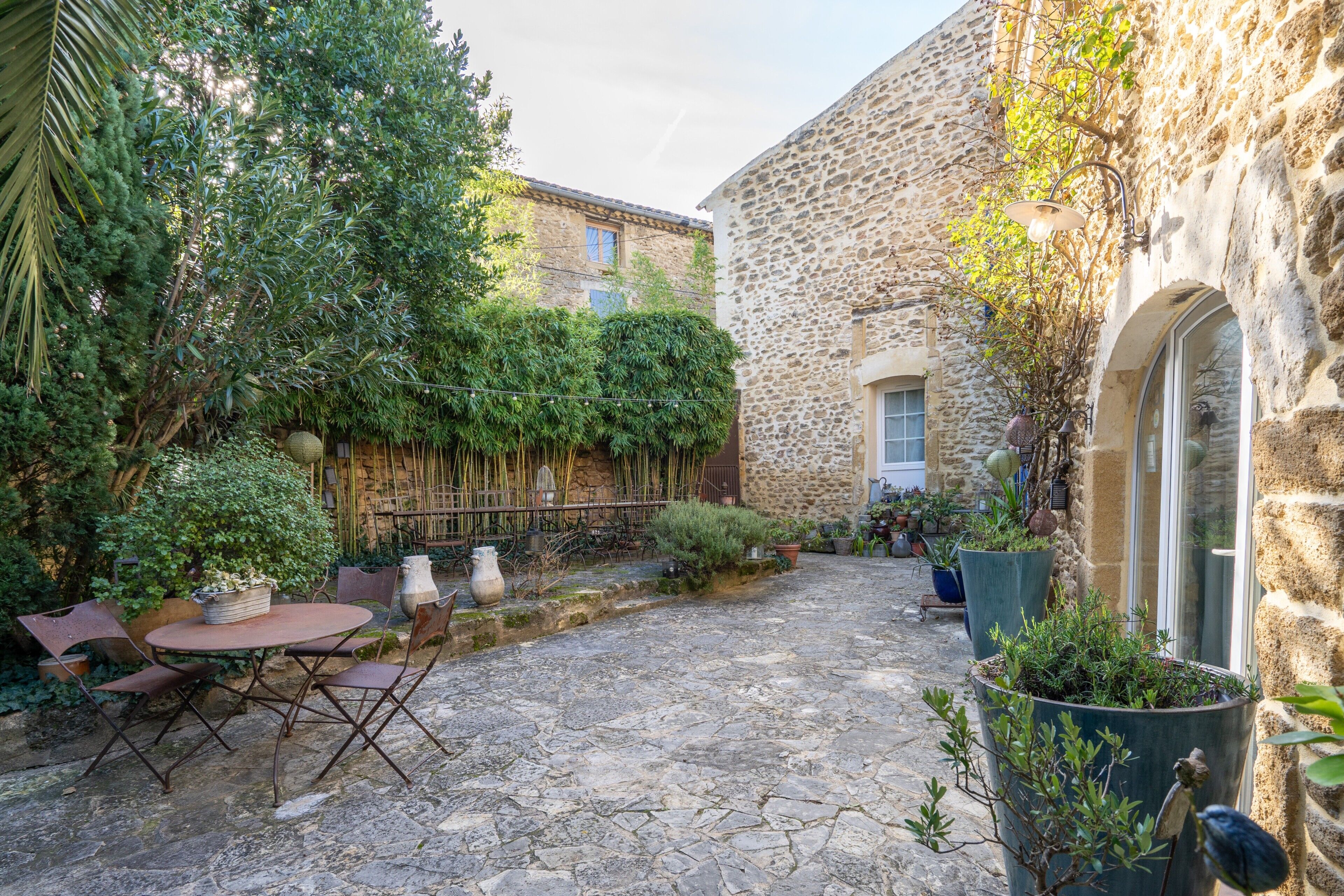 A stone courtyard with a table and chairs, surrounded by potted plants and a stone wall.