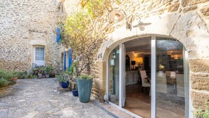 A stone building with a glass door entrance, potted plants, and a small window. - Gîte 'Les Aiguières en Provence' with Private Terrace, Private Garden and Wi-Fi (Suze-la-Rousse)