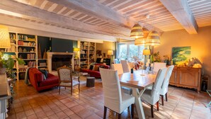 A spacious living area with a fireplace, bookshelves, a dining table with chairs, and a red sofa. - Gîte 'Les Aiguières en Provence' with Private Terrace, Private Garden and Wi-Fi (Suze-la-Rousse)